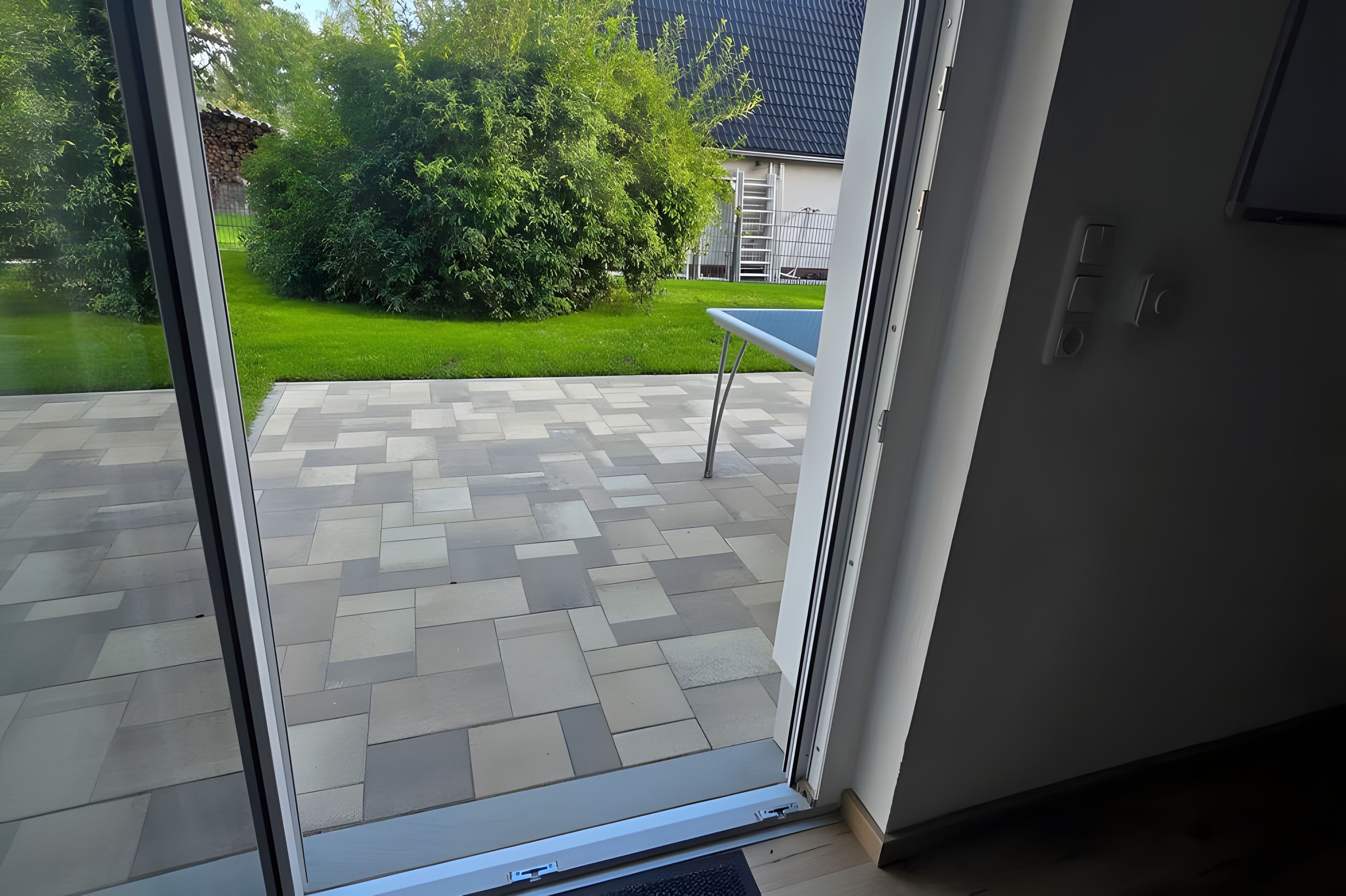 Blick durch eine Glastür in einen Patio-Bereich mit einem gemusterten Fliesenboden und einem kleinen Tisch.
