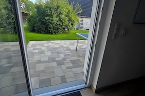 On aperçoit, à travers une porte vitrée, un patio dont le sol est recouvert de carreaux décoratifs et où se trouve une petite table.