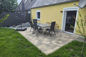 Eine Terrasse mit Tisch und Stühlen, ein kleiner Garten und ein Gebäude mit gelber Fassade.