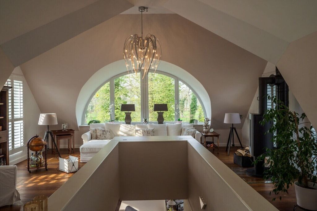 A spacious loft with a high ceiling, large windows, and a central chandelier.