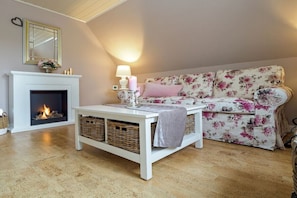A cozy living room with a fireplace, a white coffee table with baskets, and a floral sofa. - Holiday apartment Jümme (Nortmoor)