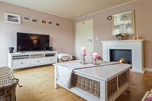 Een woonkamer met een televisie, witte meubels, een open haard en een deur.