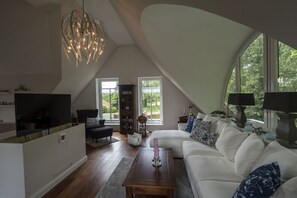 A modern living room with a white sofa, a wooden coffee table, a TV, and a unique ceiling light fixture. - Holiday apartment Jümme (Nortmoor)