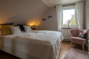 Een slaapkamer met een groot bed, een stoel, een raam met gordijnen en een radiator.