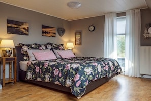 A bedroom with a bed, two bedside tables, a wall clock, and a window with curtains. - Holiday apartment Jümme (Nortmoor)