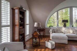 Een kamer met een witte bank, een houten kast, een wereldbol op een standaard en een raam met uitzicht op groen.