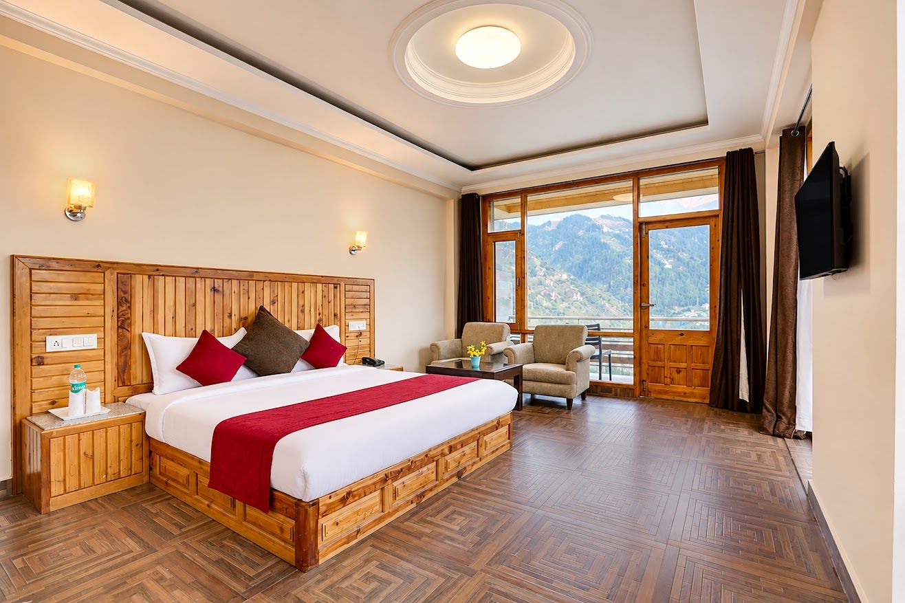 A hotel room with a large bed, wooden headboard, bedside tables, a chair, a TV, and a view of mountains.
