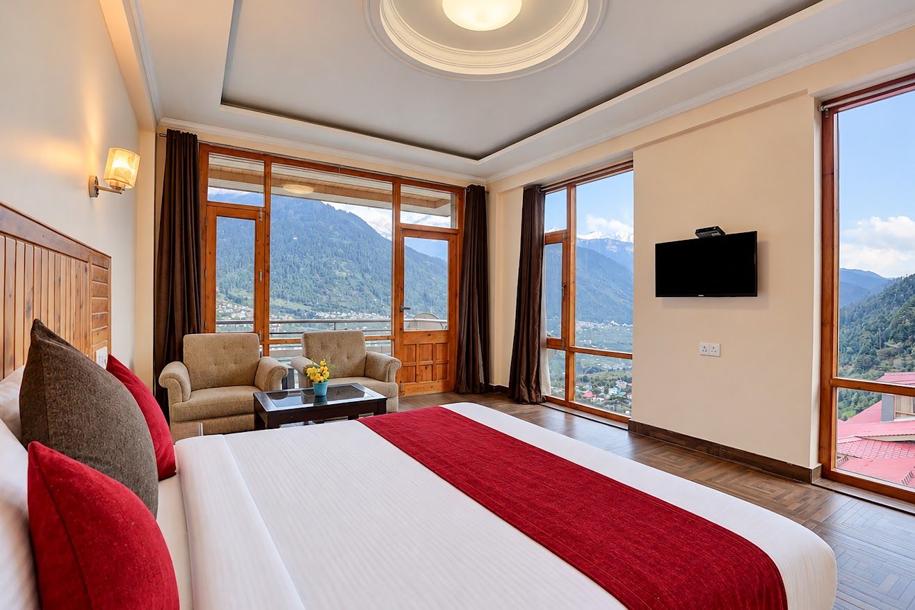 A hotel room with a large bed, a sofa, a TV, and a view of mountains.
