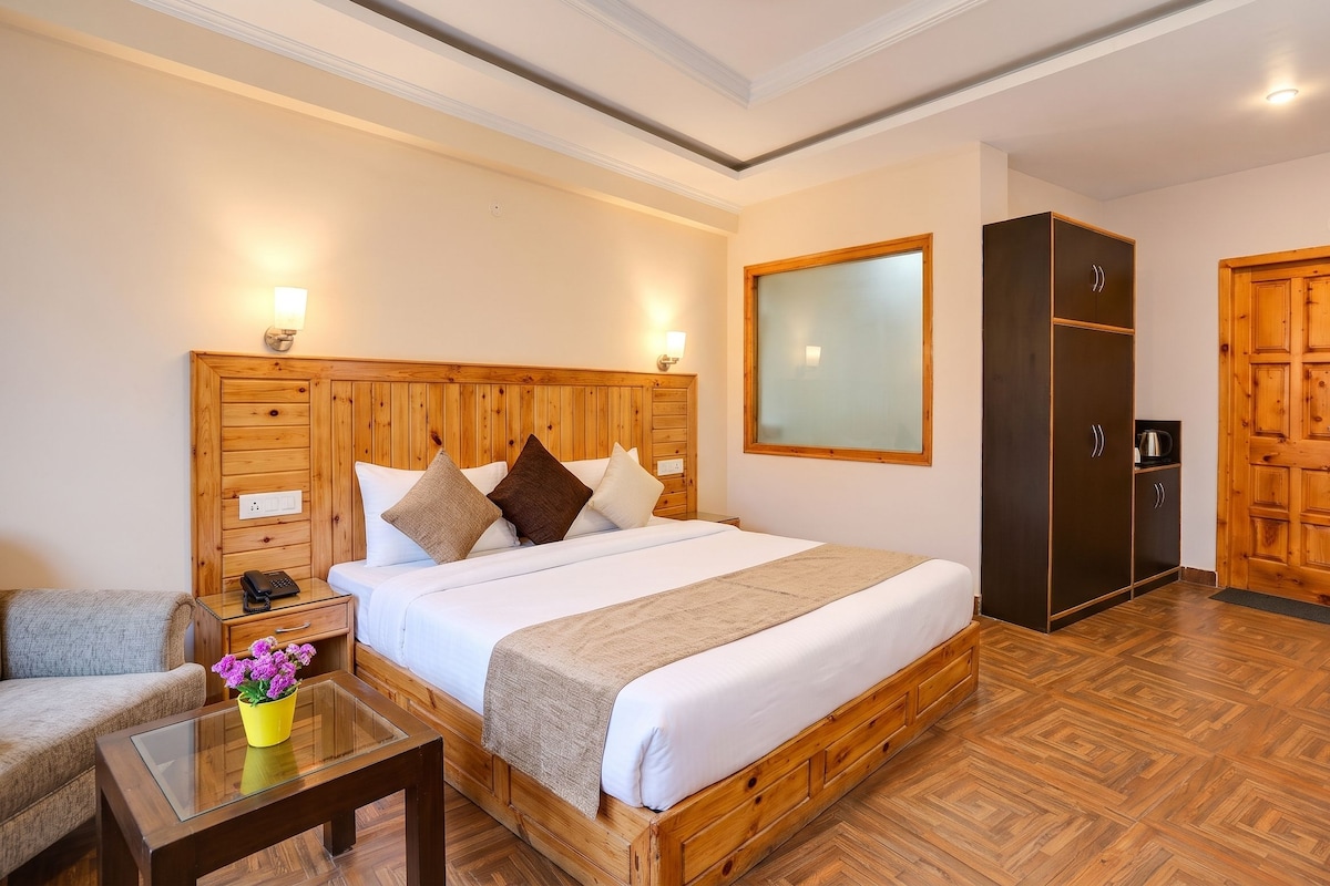 Habitación de hotel con cabecera de madera, cama con ropa de cama blanca, armario de madera, una mesita con un florero y un sofá.