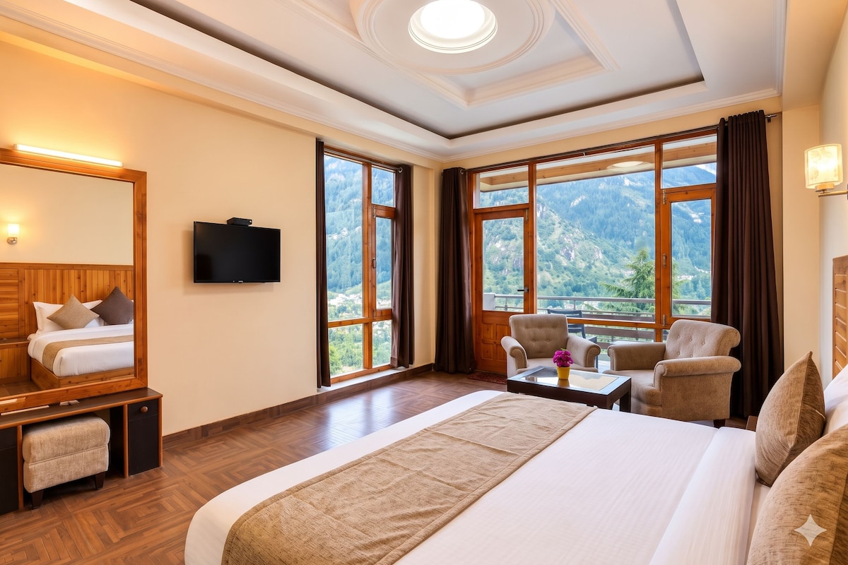 Habitación de hotel con cama, televisión, escritorio y silla. Amplias ventanas con vistas a la montaña.