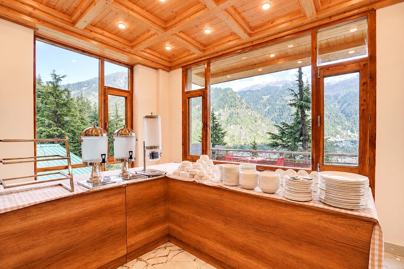A kitchen with wooden cabinets, a countertop with stacked plates, and large windows offering a mountain view.