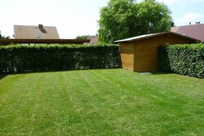 Ein gepflegter Rasen mit einem Holzschuppen und einer Hecke.