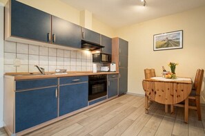A modern kitchen with dark blue cabinets, a microwave, and a dining table with chairs. - Holiday apartment Haus Vietzen 1 (Rechlin)