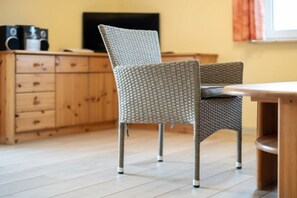 A wicker chair with a cushioned seat and backrest, positioned in front of a wooden cabinet with drawers and a flat-screen TV on top. - Holiday apartment Haus Vietzen 1 (Rechlin)