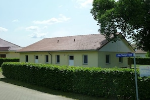 Ein zweistöckiges Gebäude mit einem Ziegeldach, einem Schild mit der Aufschrift 'Am Sumpf See' und einem Heckenbeet im Vordergrund.