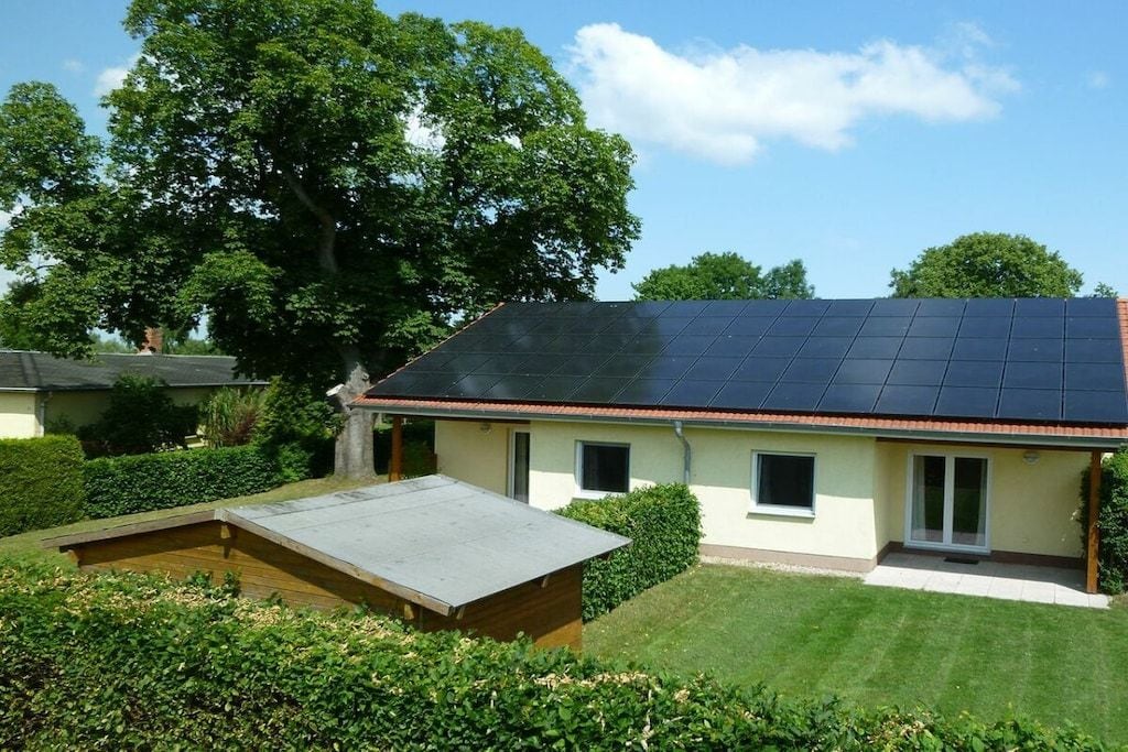 A house with a solar panel roof, a small deck, and a well-maintained lawn.