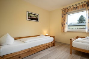 A room with two wooden beds, a window with curtains, a wall-mounted picture, and a lamp on the bedside table. - Holiday apartment Haus Vietzen 1 (Rechlin)