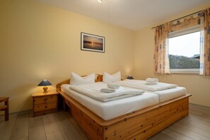 A double bed with white linens, a nightstand with a lamp, and a window with curtains. - Holiday apartment Haus Vietzen 1 (Rechlin)
