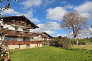 A two-story chalet with a wooden balcony, a well-maintained lawn, and a clear sky. - Holiday apartment with 1 bedroom (Füssen-Hopfen am See)