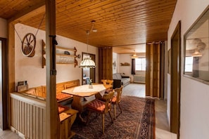 A wooden dining area with a table and chairs, a radiator, and a patterned rug. - Holiday apartment with 1 bedroom (Füssen-Hopfen am See)