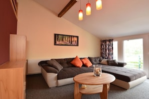 A cozy living room with a sectional sofa, a small wooden table, and a painting on the wall. - Holiday home with 3 bedrooms (Ilmtal \/ OT Traßdorf)