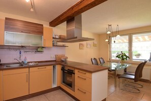 A modern kitchen with wooden cabinets, a built-in oven, and a dining area with a glass table and chairs. - Holiday home with 3 bedrooms (Ilmtal \/ OT Traßdorf)