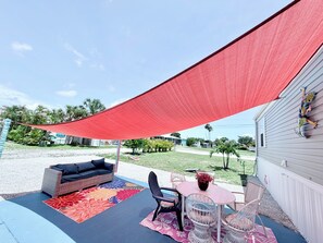 A covered patio area with outdoor furniture, a colorful rug, and a view of the surrounding neighborhood. - Manatee Sisters-2 Gulf cottages steps apart +2 Docks/Private community pool/spa (Saint James City)