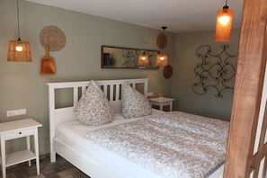 Ein Schlafzimmer mit einem weißen Bett, Kissen mit Muster, einem Nachttisch und Wanddekoration.