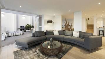Un salon moderne avec un canapé gris aux lignes courbes, une table basse ronde en verre et un tapis à motifs.