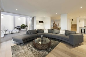 Een moderne woonkamer met een gebogen grijze bank, een ronde glazen salontafel en een rug met een patroon.