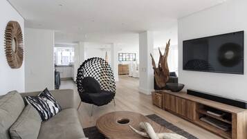 Un salon moderne avec un canapé, un fauteuil noir, une table basse en bois et un téléviseur fixé au mur.