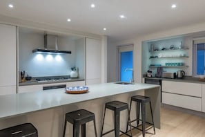 A modern kitchen with a central island, bar stools, and built-in shelves. - 26 Geneva Drive - Sandpiper House (Cape Town)