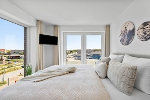 A hotel room with a large bed, a sofa, a flat-screen TV, and a view of the outside. - Holiday apartment with 1 bedroom (Dagebüll)