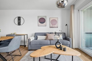 A modern living room with a grey sofa, a wooden coffee table, and a round mirror on the wall. - Holiday apartment with 1 bedroom (Dagebüll)