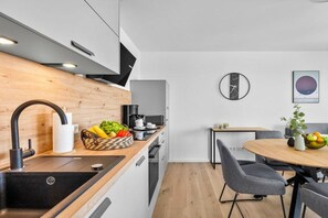 A modern kitchen with a wooden countertop, a black sink, and a dining area with a round table and grey chairs. - Holiday apartment with 1 bedroom (Dagebüll)
