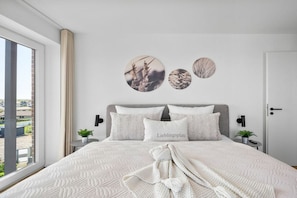 Ein Schlafzimmer mit einem großen Bett, Blick ins Freie und drei Wanddekorationen in runder Form.