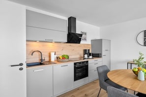A modern kitchen with grey cabinets, a wooden countertop, a black range hood, a built-in oven, and a dining area with a round table and grey chairs. - Holiday apartment with 1 bedroom (Dagebüll)