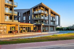 Un immeuble à plusieurs étages doté de balcons, d’un espace extérieur aménagé avec des sièges et d’un jardin paysager à l’avant.