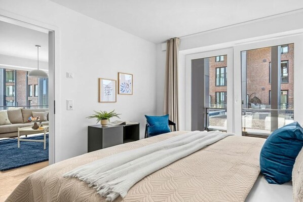 Et moderne hotelværelse med en stor seng, en sofa, et lille bord og udsigt over byen gennem store vinduer.