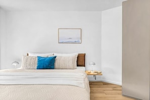 A bedroom with a bed, pillows, a bedside table with a lamp, and a framed picture on the wall. - Holiday apartment with 1 bedroom (Dagebüll)