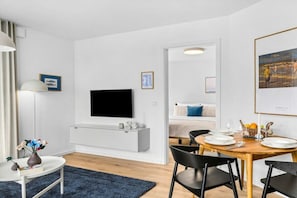Un saló modern amb televisió de pantalla plana, una zona de menjador amb taula de fusta i cadires negres, i un espai d'estar acollidor amb una catifa blava.