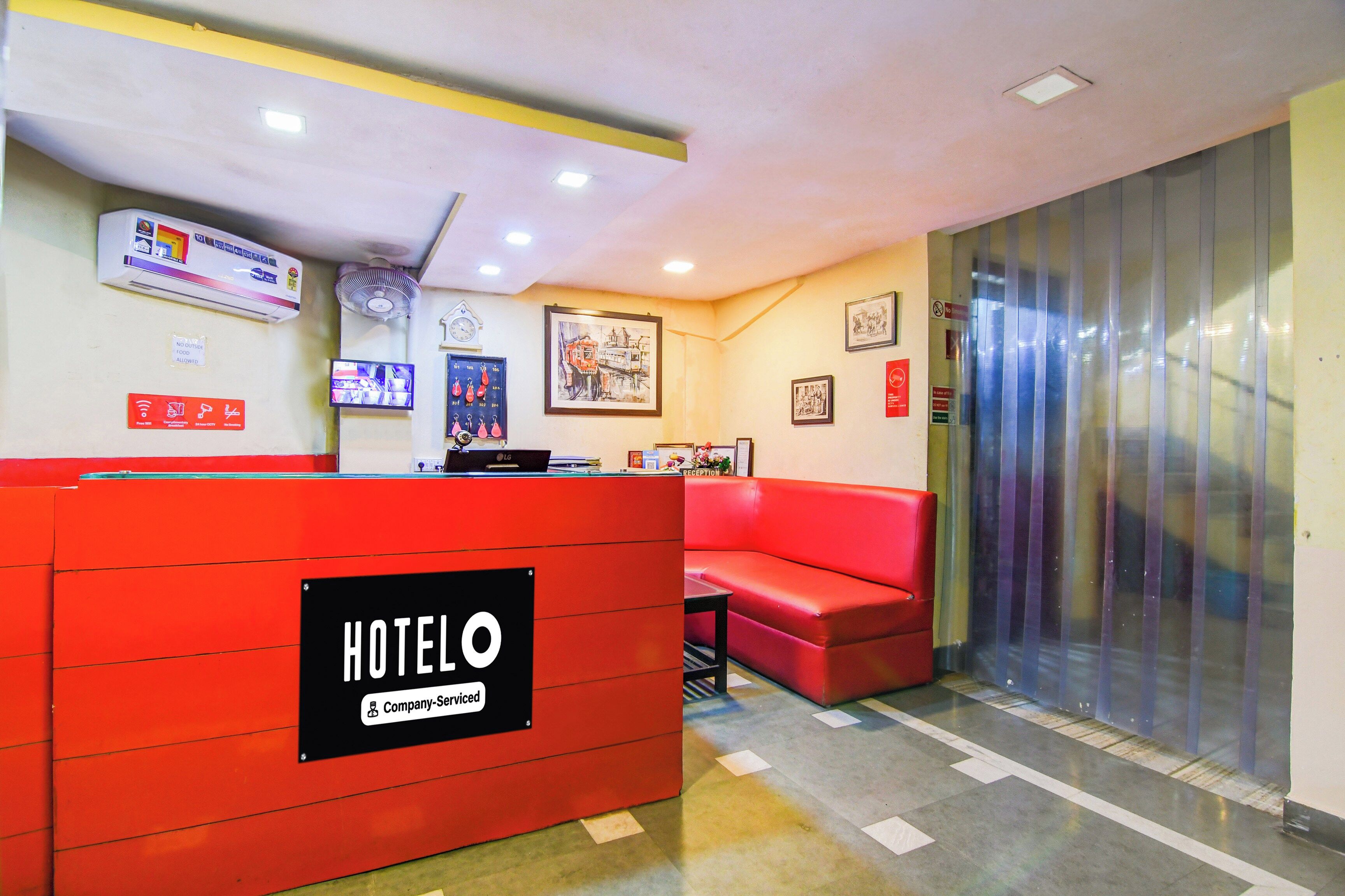 Zona de recepción de un hotel con un mostrador rojo, un área de estar con un sofá rojo y un reloj en la pared.