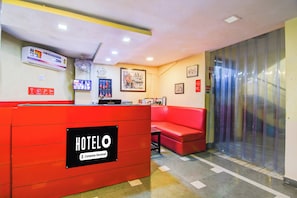 Uma área de recepção de hotel com um balcão vermelho, um espaço de estar com sofá vermelho e um relógio fixado na parede.