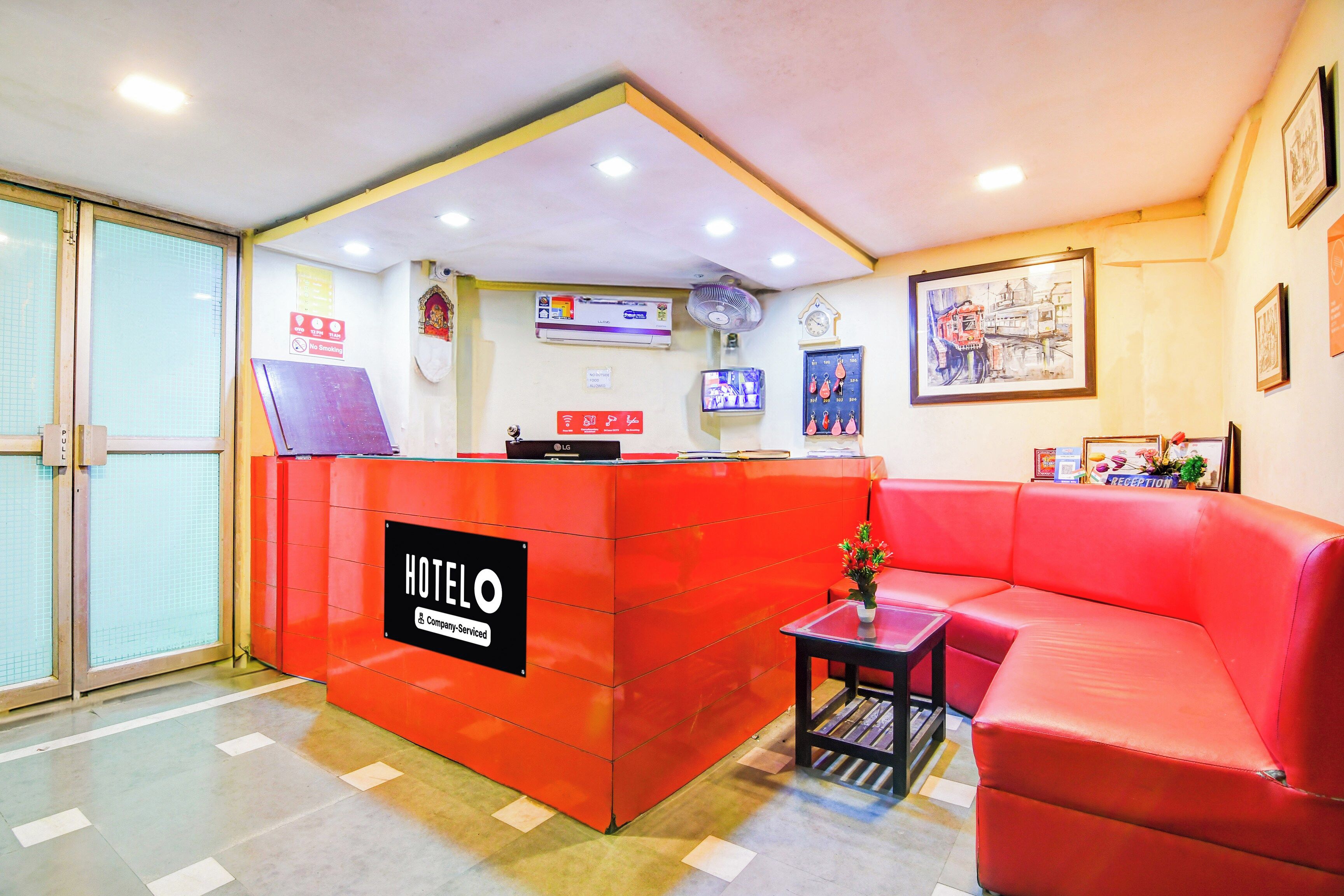 Una recepción de hotel con un sofá rojo y una pequeña mesa, un reloj y un cuadro en la pared.