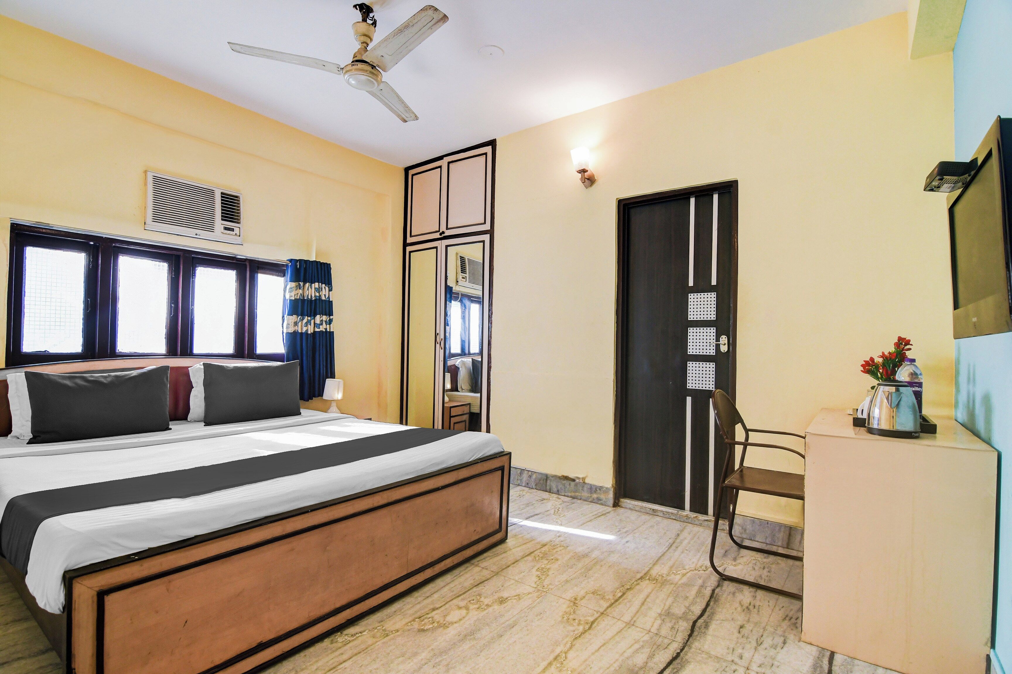 Habitación de hotel con cama, escritorio, silla, ventilador de techo y puerta con cerradura de seguridad.