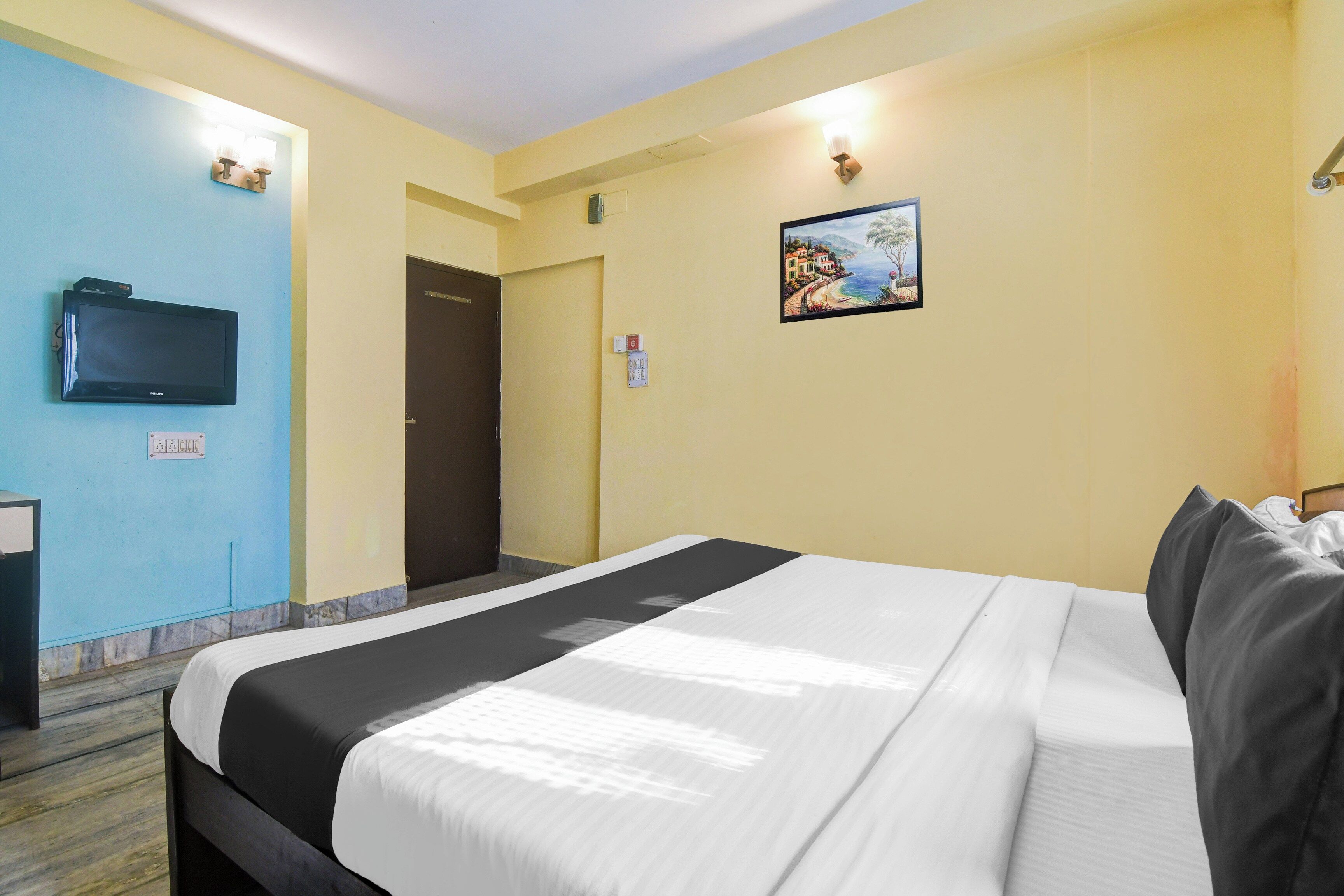 Habitación de hotel con cama, televisor, puerta y lámpara fijada a la pared.
