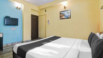 Habitación de hotel con cama, televisor, puerta y lámpara fijada a la pared.