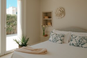 A bedroom with a bed, a bedside table with books, a wall-mounted shelf, and a view of greenery outside. - Sea Loft  (Puglia)