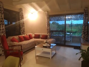 Ein Wohnzimmer mit einer Couch, Sesseln, einem Couchtisch und Blick ins Freie durch eine Glastür.