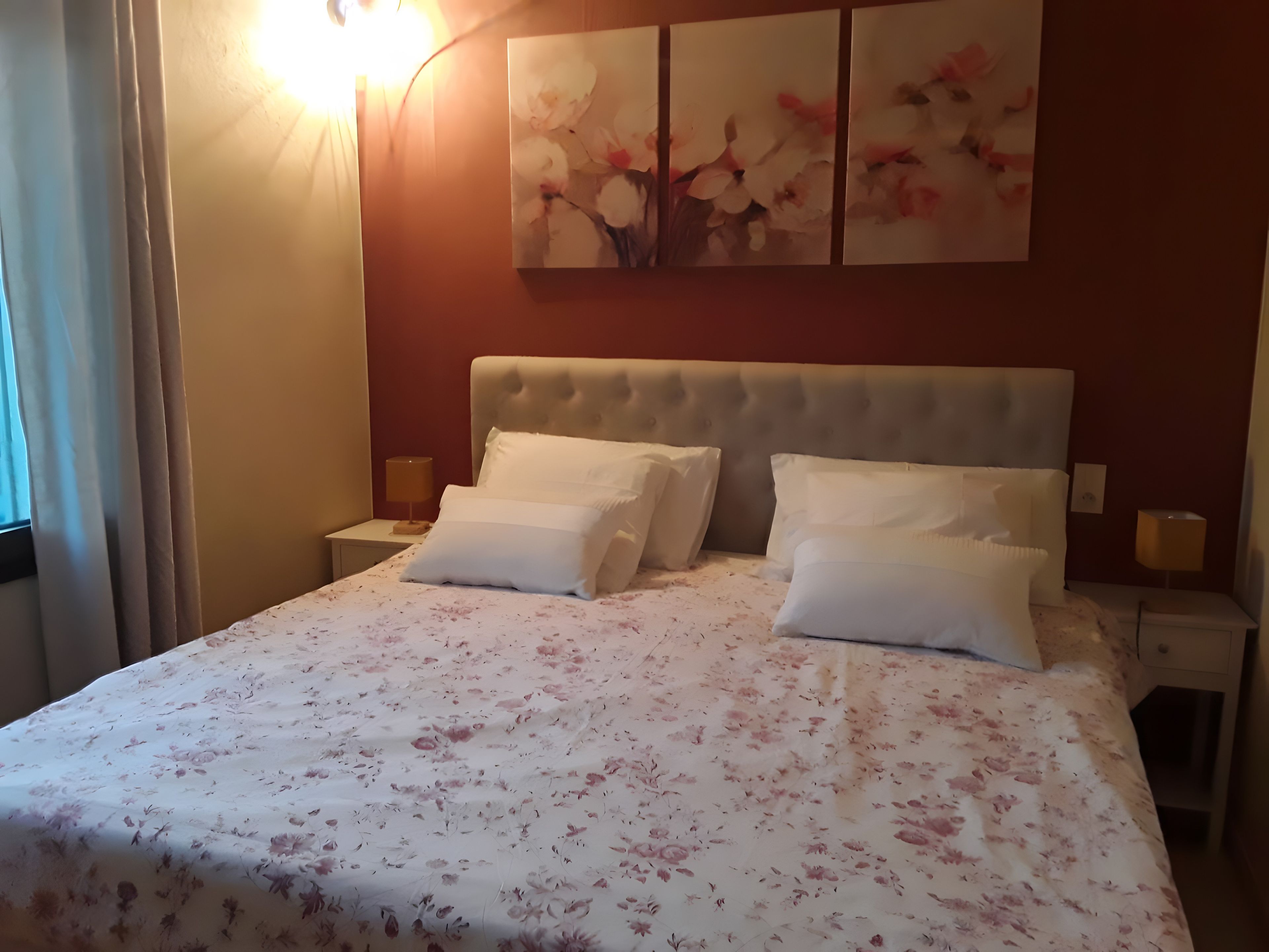 A hotel room with a large bed, two bedside tables, a wall-mounted artwork, and a window with curtains.
